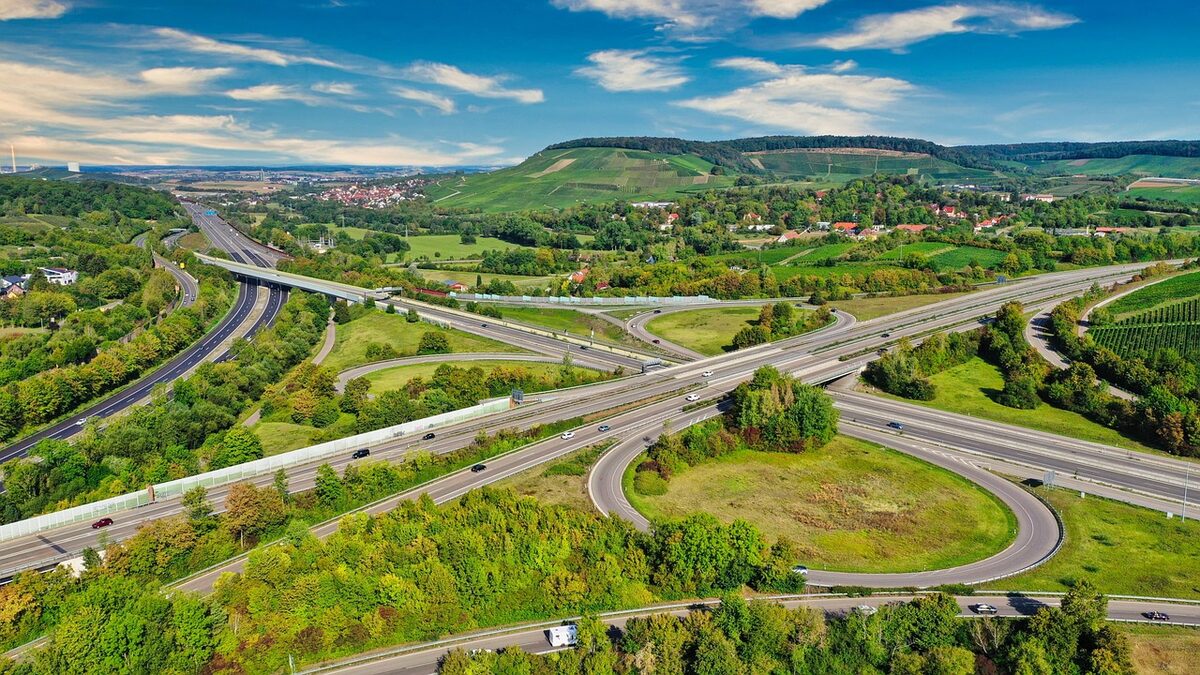 Luftaufnahme eines Autobahnkreuzes, dessen Verbindungsrampen sich zwischen Feldern und Waldstücken verzweigen