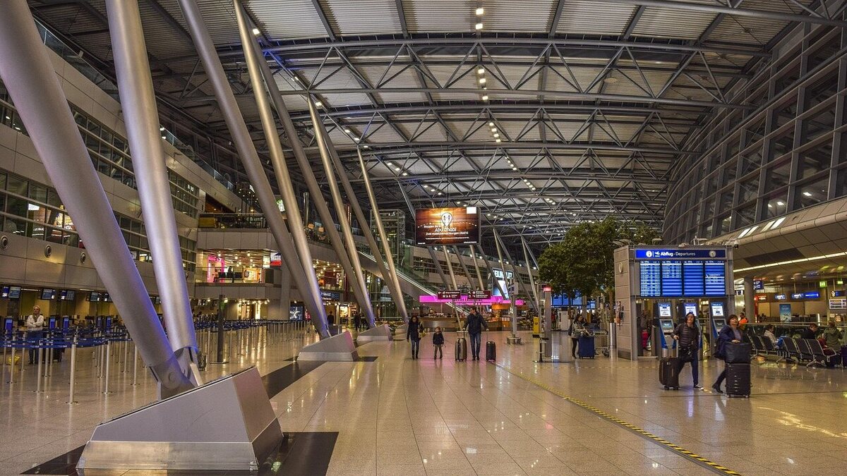 Abflughalle eines Flughafen-Terminals mit Anzeigetafeln und wartenden Reisenden mit Koffern