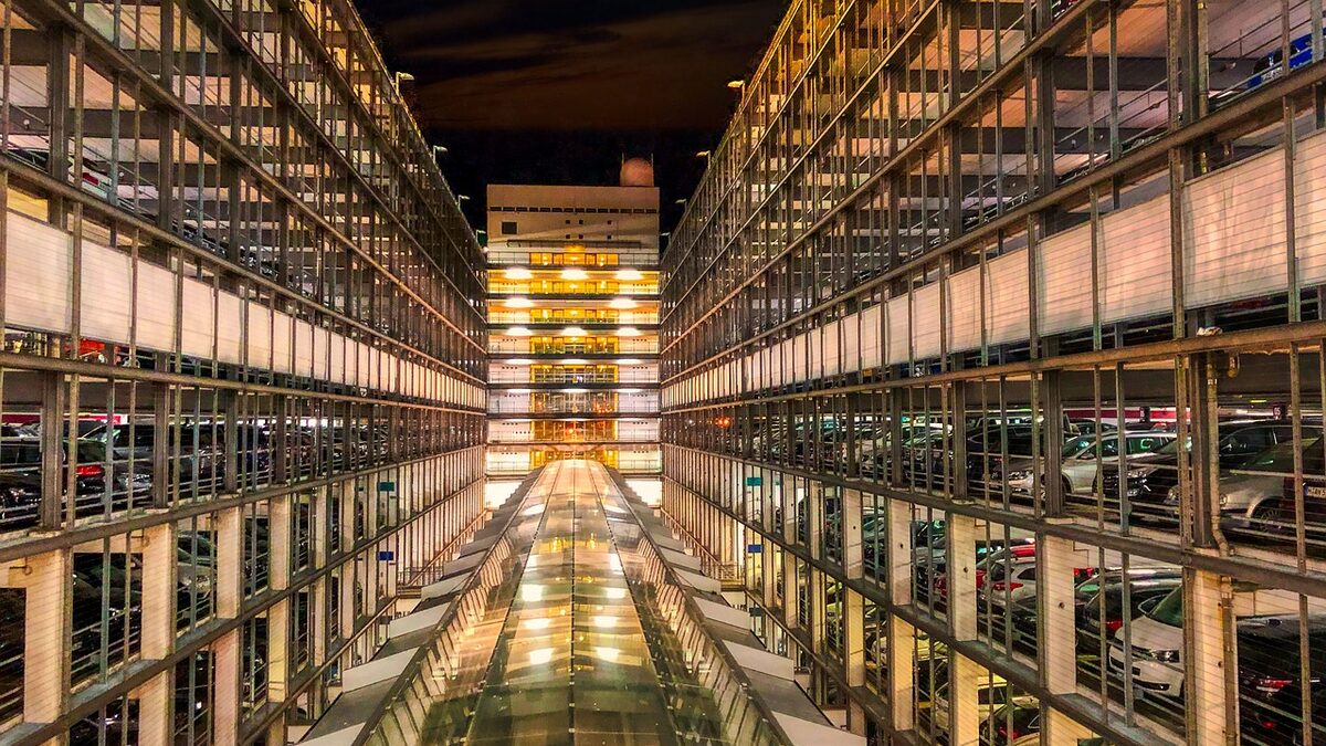 Mehrgeschossiges Parkhaus in der Abenddämmerung, hinter den offenen Fassadengittern stehen auf jeder Ebene Fahrzeuge