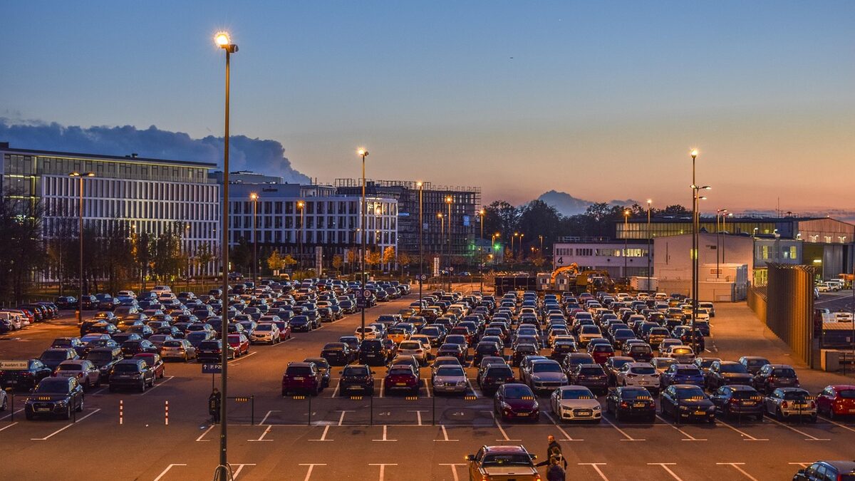 Großer Parkplatz mit dicht belegten Stellplatzreihen, beleuchtet von Mastleuchten in der Abenddämmerung