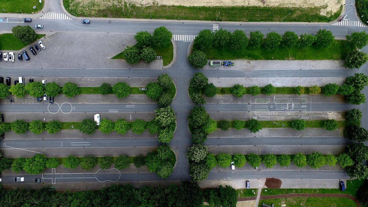 Senkrechte Luftaufnahme eines Parkplatzes, dessen lange Stellplatzreihen durch Baumreihen voneinander getrennt sind