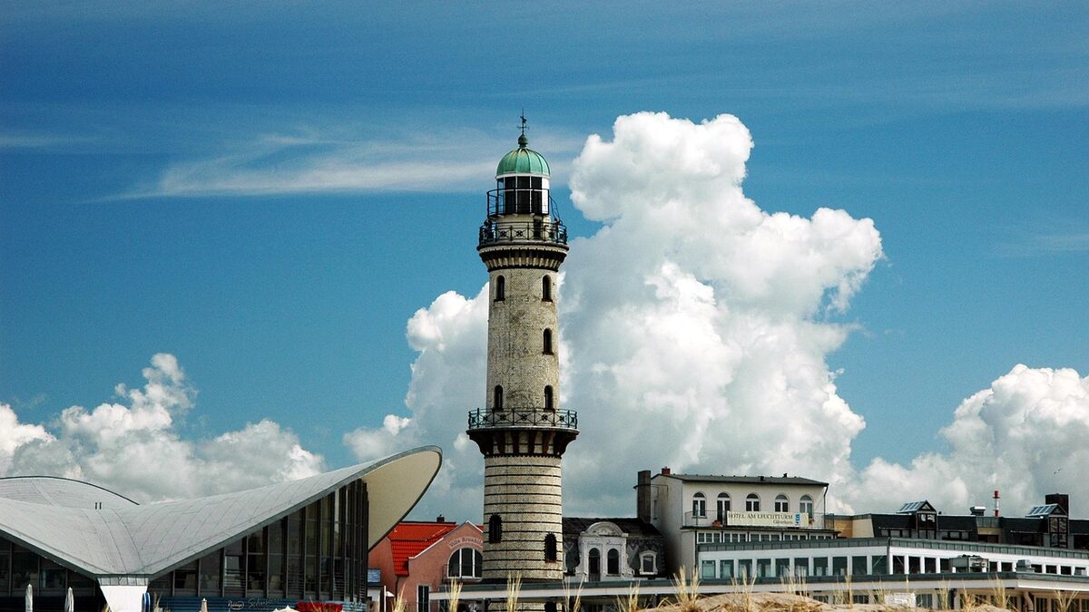 Der Leuchtturm von Warnemünde und das geschwungene Dach des Teepotts vor aufgetürmten Schönwetterwolken