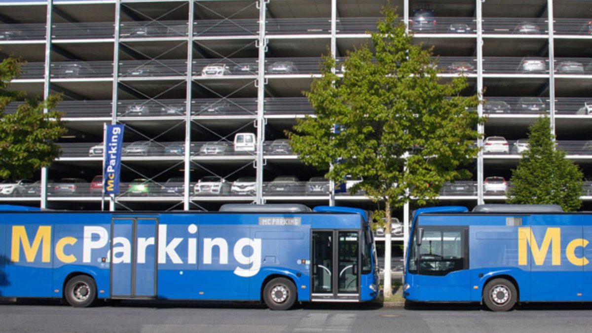 Zwei blaue McParking-Shuttlebusse stehen hintereinander vor dem mehrgeschossigen Parkhaus des Betriebs am Flughafen BER