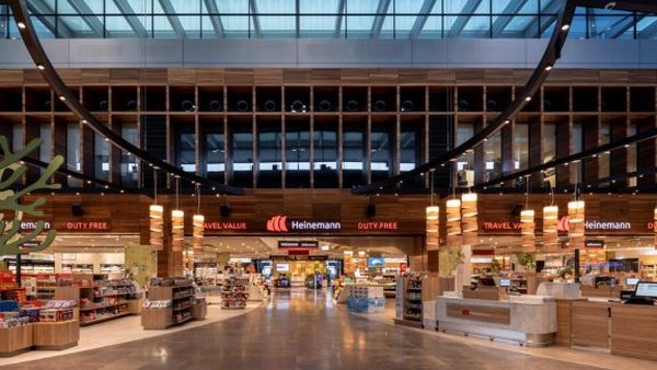 Weit geöffnete Ladenfront der Heinemann-Shops im Terminal des Flughafens BER mit beleuchteten Schriftzügen „Duty Free" und „Travel Value" unter einer Holzlattendecke